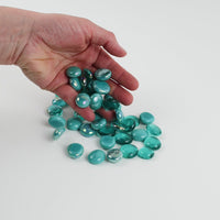 Video of green-blue mix glass nuggets in teal and aqua shades with an iridescent sheen, 16–20 mm, picked up from a pile by hand and dropped back to show their size, round shape and shine