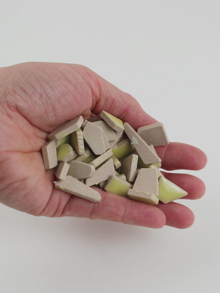 Video of Flip ceramic puzzle pieces in ochre yellow, opaque glazed porcelain, 4–20 mm, held in a hand and poured out to show their shapes and finish